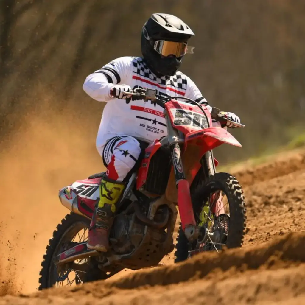 Pascal Klingebiel (MSC Geisleden) auf einem roten Motocross-Bike in voller Rennmontur mit weißem Trikot, Helm und Brille, rast über einen staubigen Lehmkurs.